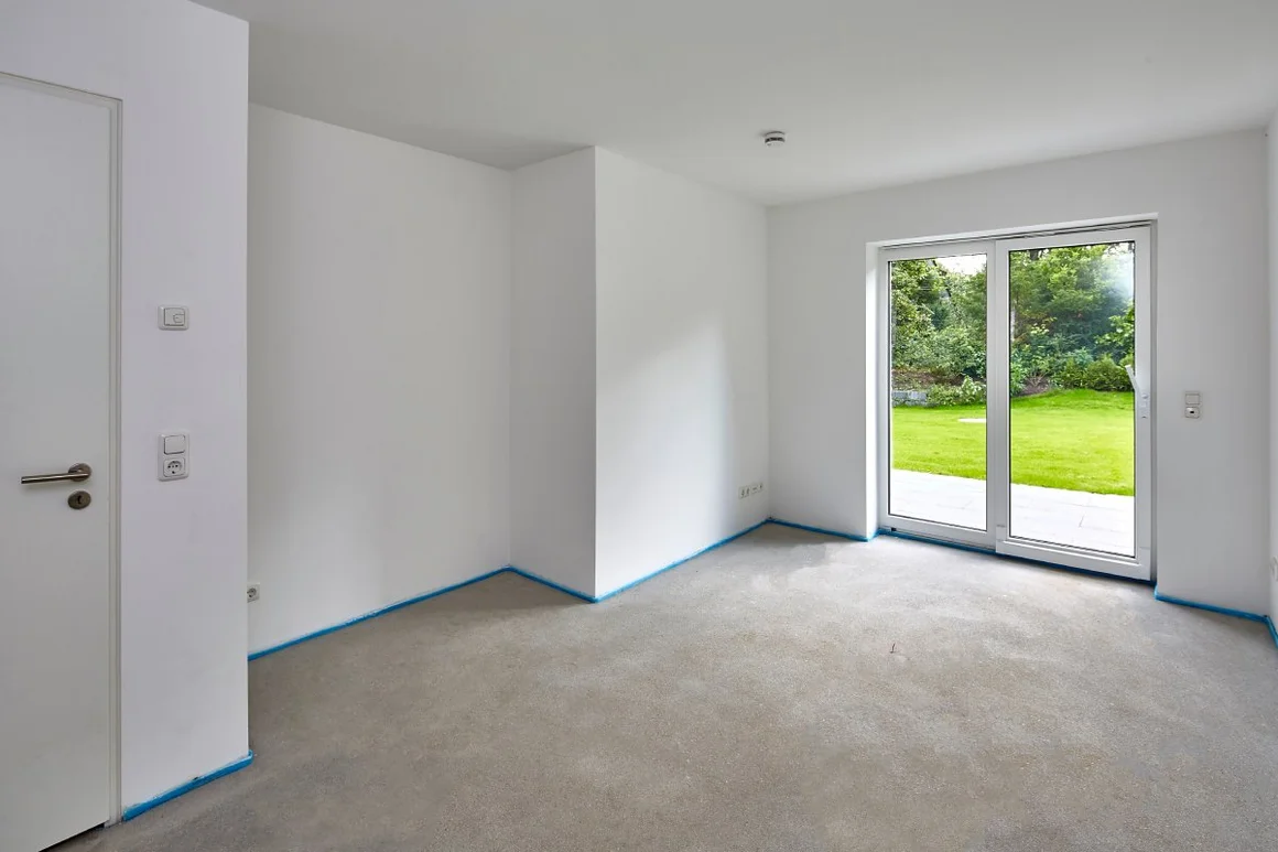 Leerer Raum mit Estrich und Blick in den Garten.